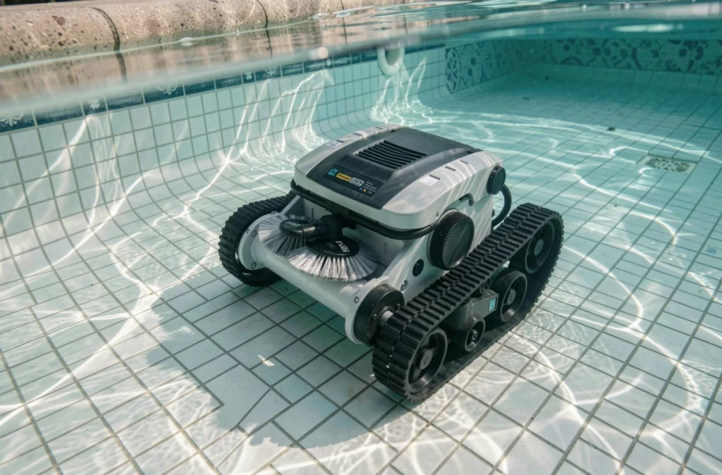 Robot hydraulique de nettoyage en train de circuler sur le fond d'une piscine résidentielle aux carrelages blancs et à l'eau translucide